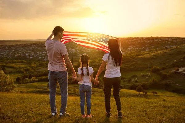 A family holding an American flag together at sunset