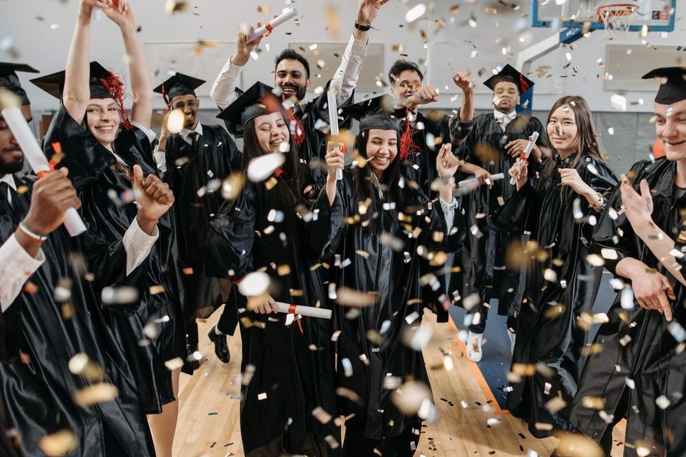 Graduates celebrating together in caps and gowns with confetti