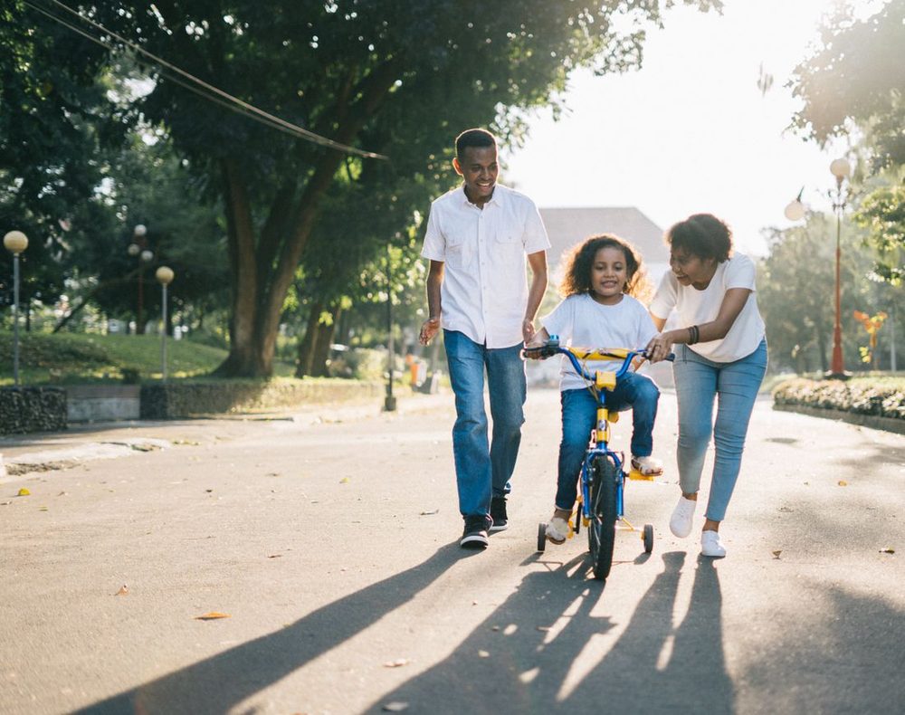 Parents teaching their daughter to ride a bike in a sunlit park
